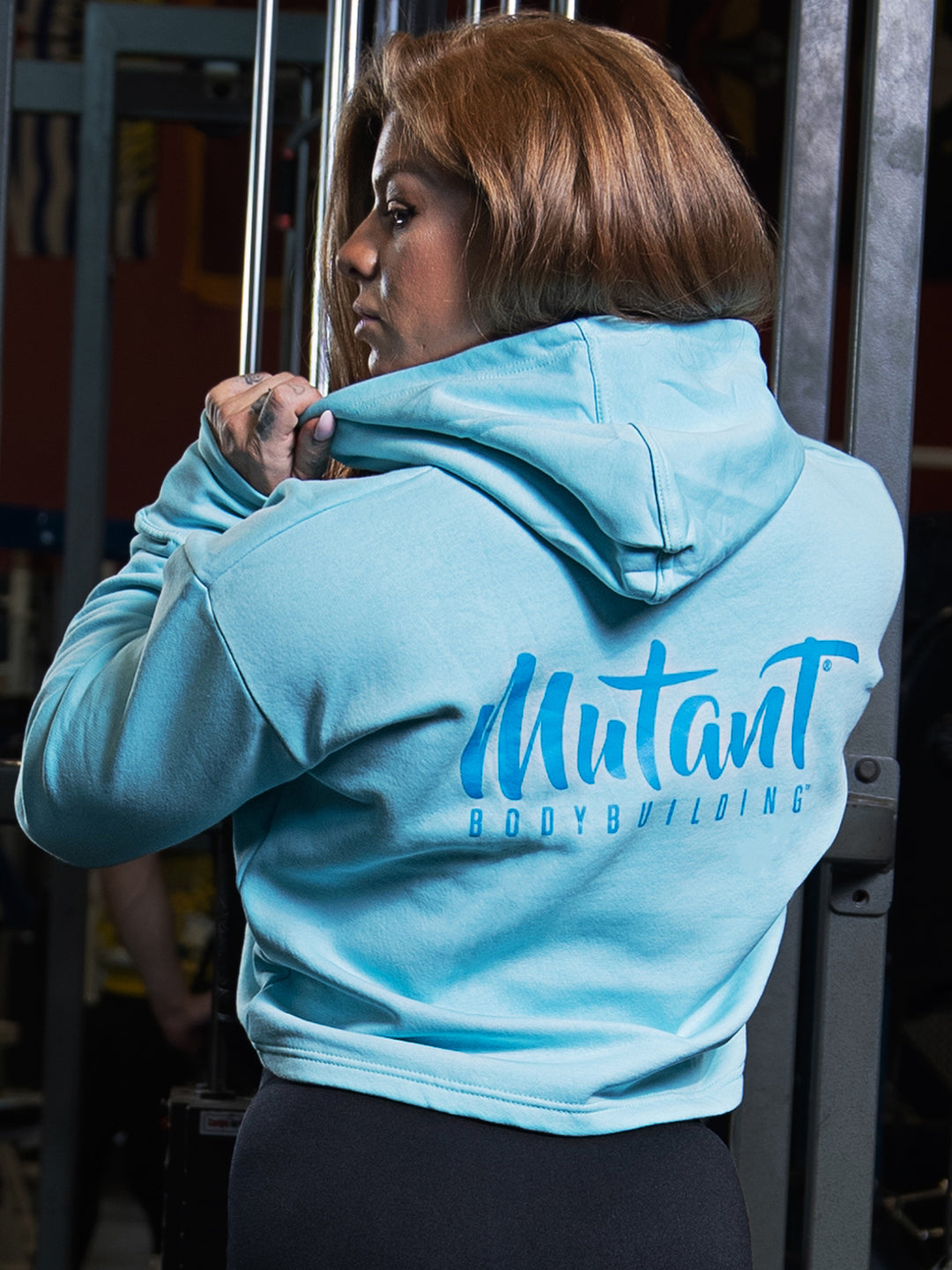 Shelby Guillaume, Mutant athlete, posing in the gym to showcase the back of the Sky Blue Mutant Thick Script Women's Gym Crop Hoodie.