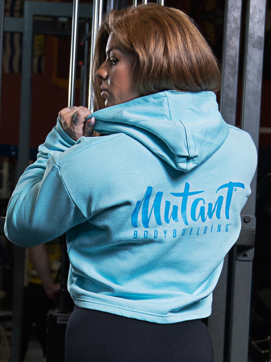 Shelby Guillaume, Mutant athlete, posing in the gym to showcase the back of the Sky Blue Mutant Thick Script Women's Gym Crop Hoodie.