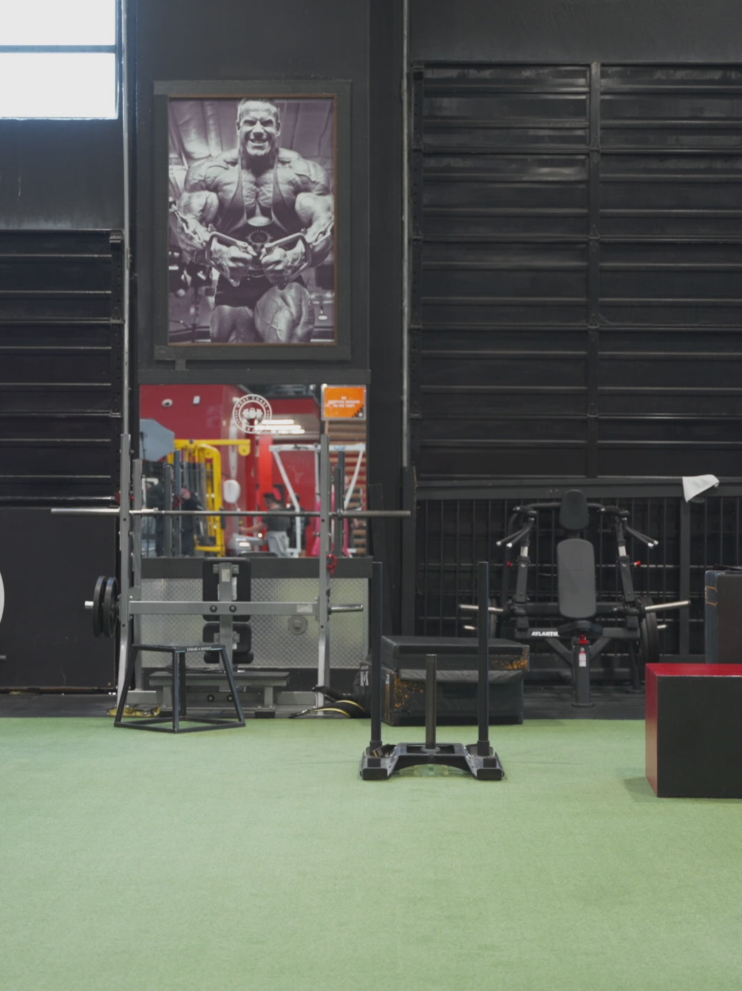 A video featuring Dana Baker at the gym, posing to display both the front and back of the red 'MUTANT's Truck Month' t-shirt that has the 'Like a Mutant' slogan and the 'Leave Humanity Behind' tagline printed in black.